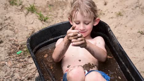 young boy playing in mud in wheelbarrow filled with water