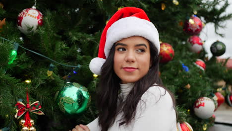 una joven feliz con un sombrero de santa celebrando la navidad y la temporada navideña con un árbol festivo y adornos