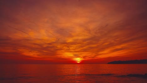 cinemagraph / seamless video loop of a vibrant red sunset at a remote natural tuscany seaside sand beach in italy with dramatic sky and panoramic sea view. blue and turquoise water at the scenic nature tourist vacation location.