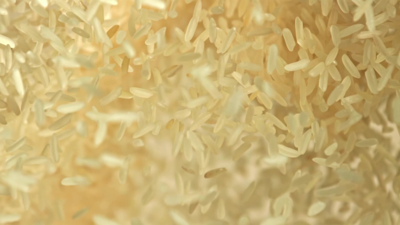 Versamento al rallentatore di chicchi di riso bianco su sfondo beige