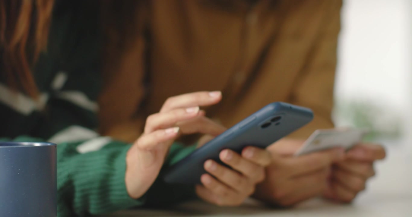 African American couple at table, woman in green sweater tapping blue phone as man holding card