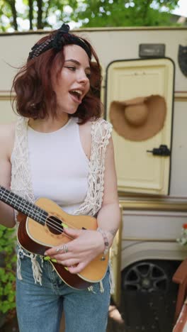 happy woman playing ukulele by camper van