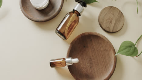 Close-up-of-glass-bottles,-cream-tub-and-wooden-plates-with-copy-space-on-grey-background