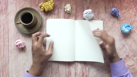 manos trabajando en un cuaderno con café y papeles arrugados