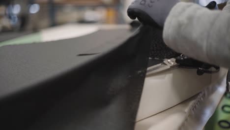 Closeup-shot-of-a-worker-using-fabric-scissors-to-trim-black-fabric-around-upholstered-furniture