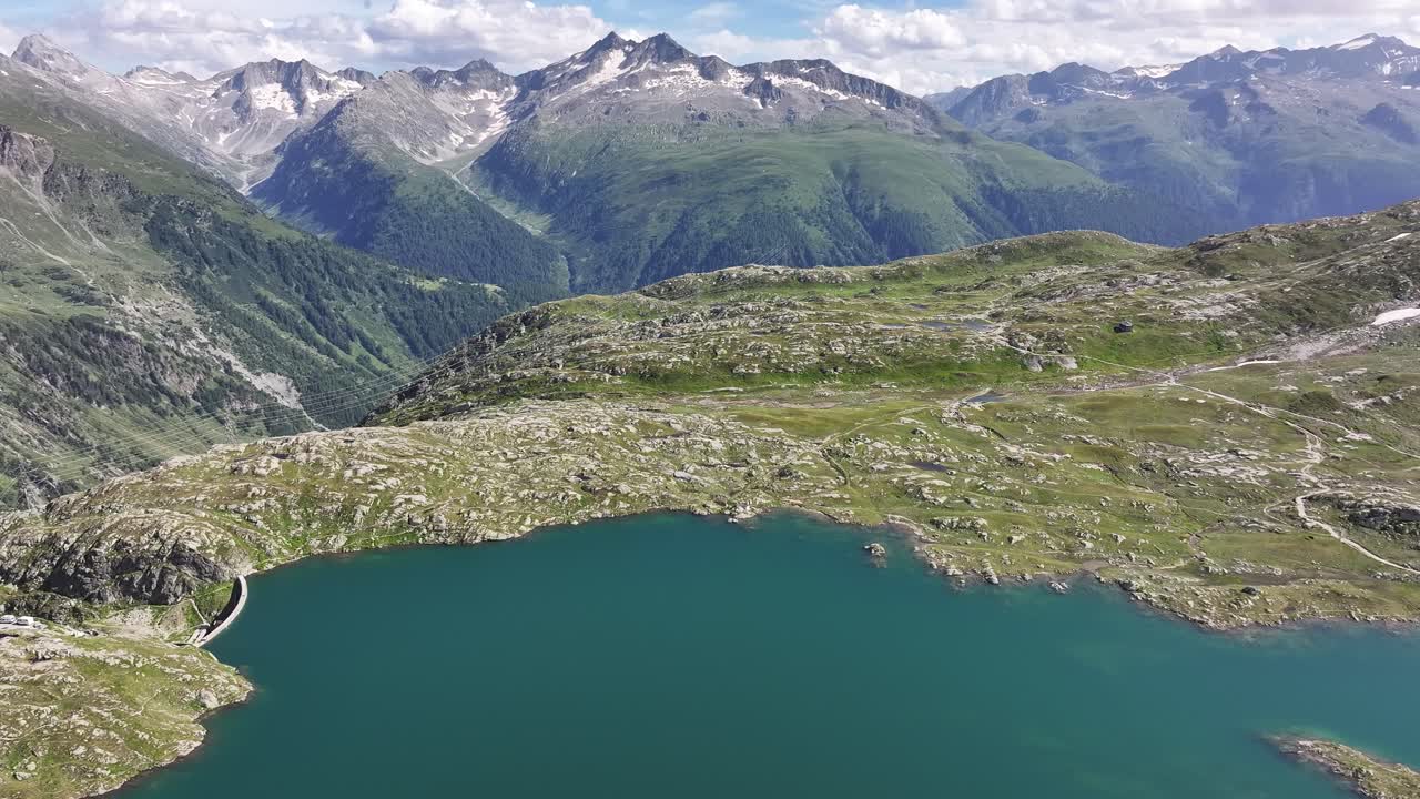 드론이 스위스 그림젤파스 산맥을 배경으로 한 산 호수 위를 날아다닙니다.