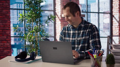 man seated at home office desk using computer, checking emails