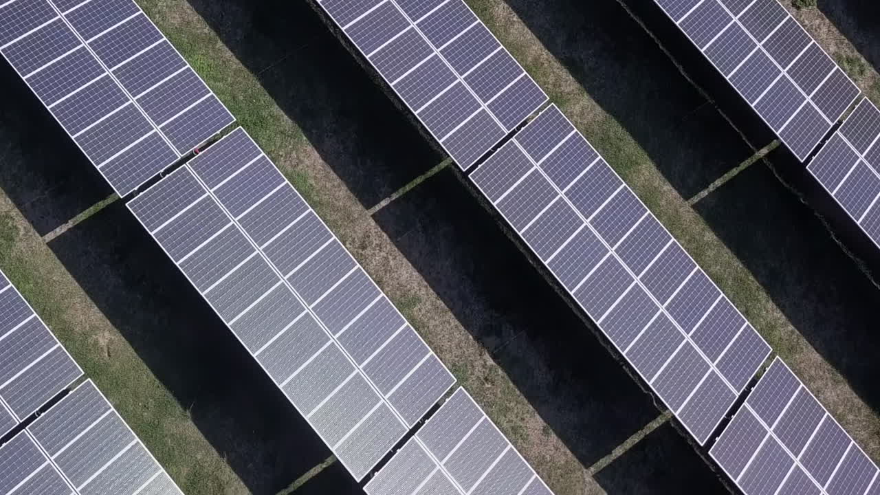 Sorvolo aereo verticale su un vasto schieramento di pannelli solari, giornata di sole.
