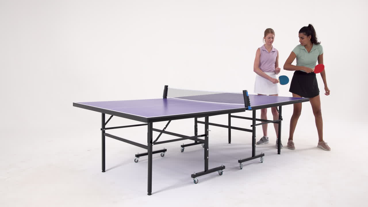 Playing table tennis, two women holding paddles and standing near table