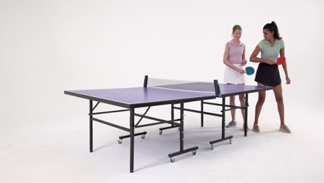 playing table tennis, two women holding paddles and standing near table