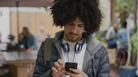 retrato de un joven de raza mixta, un estudiante que envía mensajes de texto, navega en línea usando un teléfono inteligente, medios sociales, parece pensativo en el fondo de una ciudad urbana