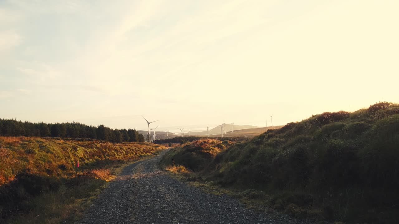 Landscape view of a dirt road through a windmill farm, producing green energy, cloudy and windy, at sunrise