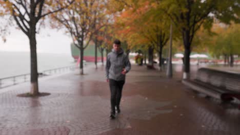 Young-Caucasian-male-with-attitude-walks-towards-camera,-pulls-up-hood-in-the-rain-downtown-Toronto