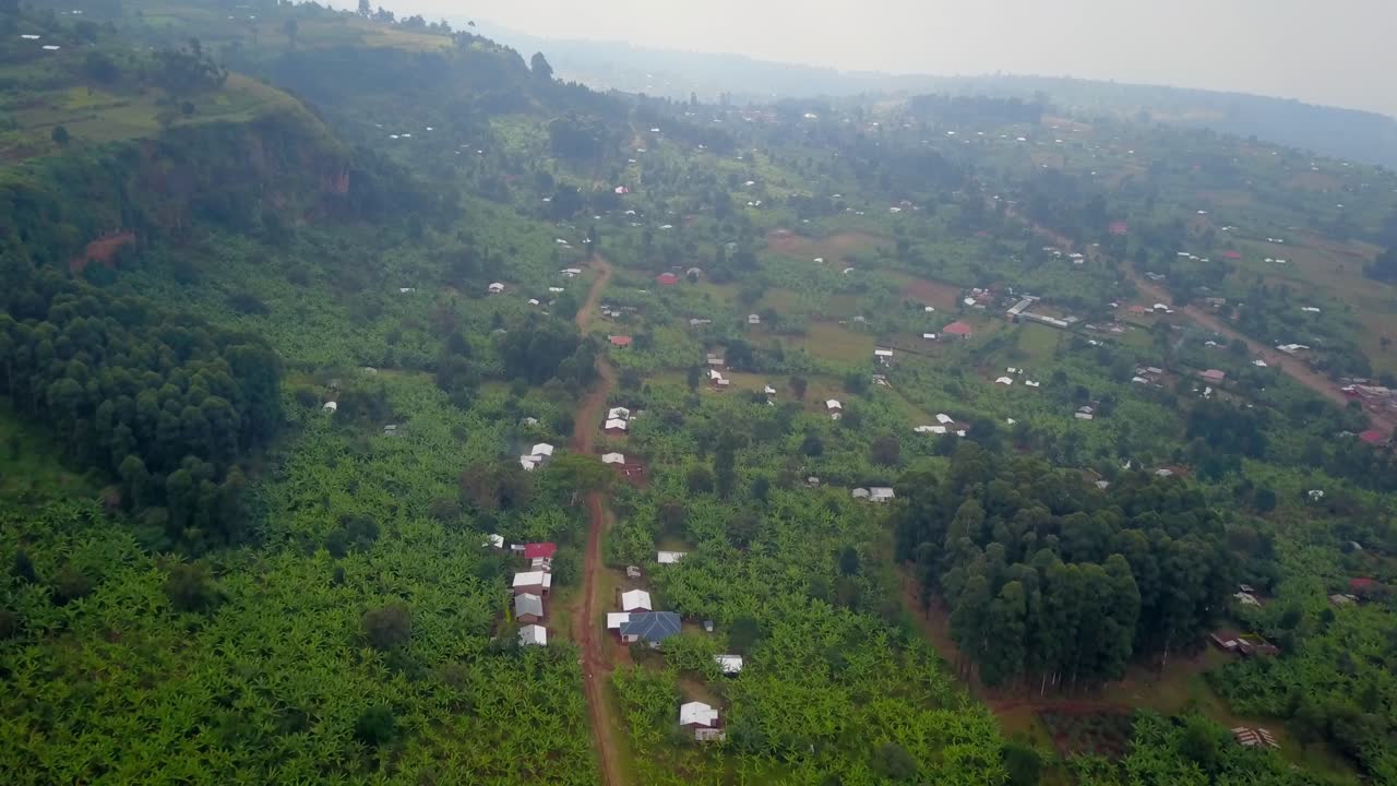 Aerial view of Kapchorwa Town, Uganda, with scattered houses, banana plantations, and thick forest patches set against the undulating green terrain at the base of Mount Elgon