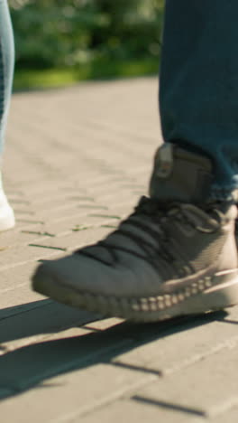 vista lateral de piernas en movimiento en un camino entrelazado, individuos con zapatillas y botas caminando juntos, con vegetación y estructuras urbanas suavemente borrosas en el fondo
