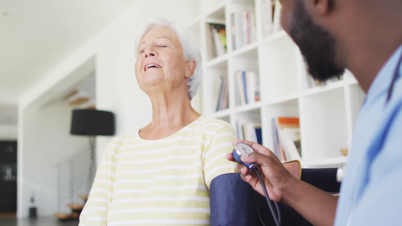 Video of african american male doctor checking pressure to caucasian senior woman