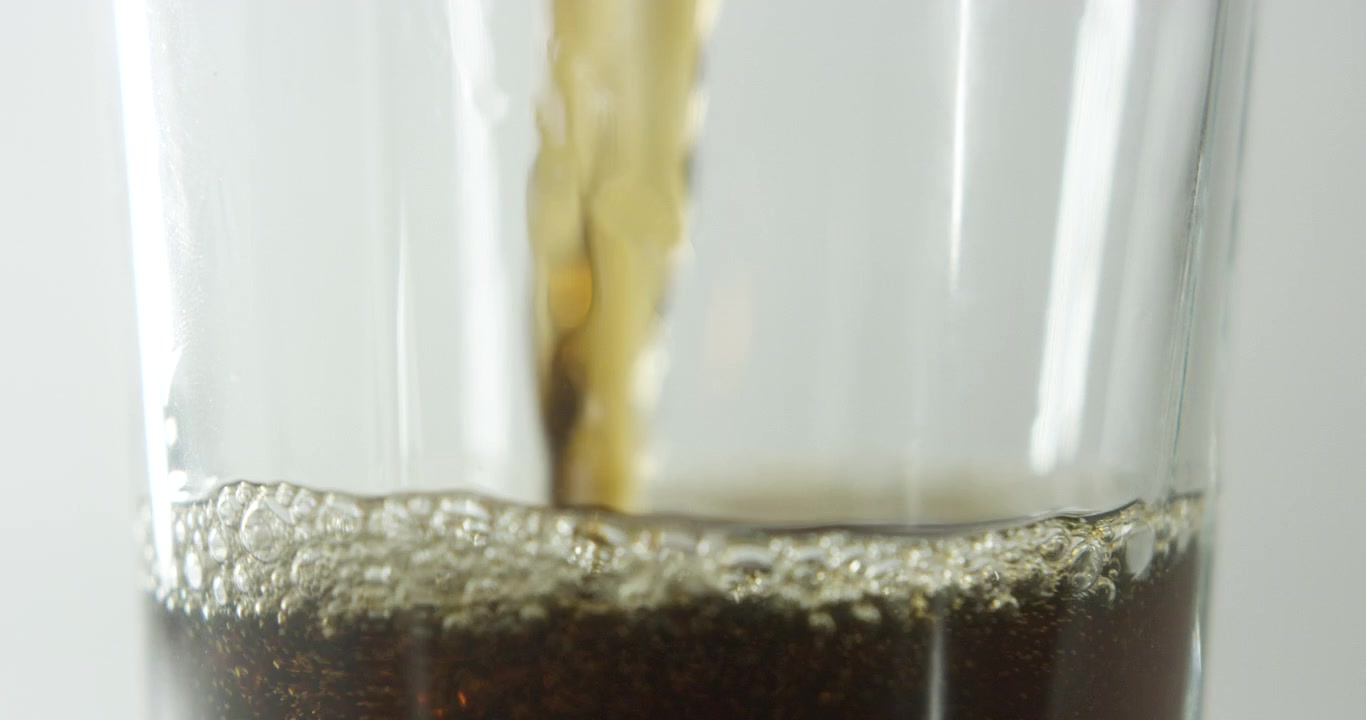 Phần giữa của một ly đang được đổ đầy đồ uống cola, quay chậm trên nền sáng rõ