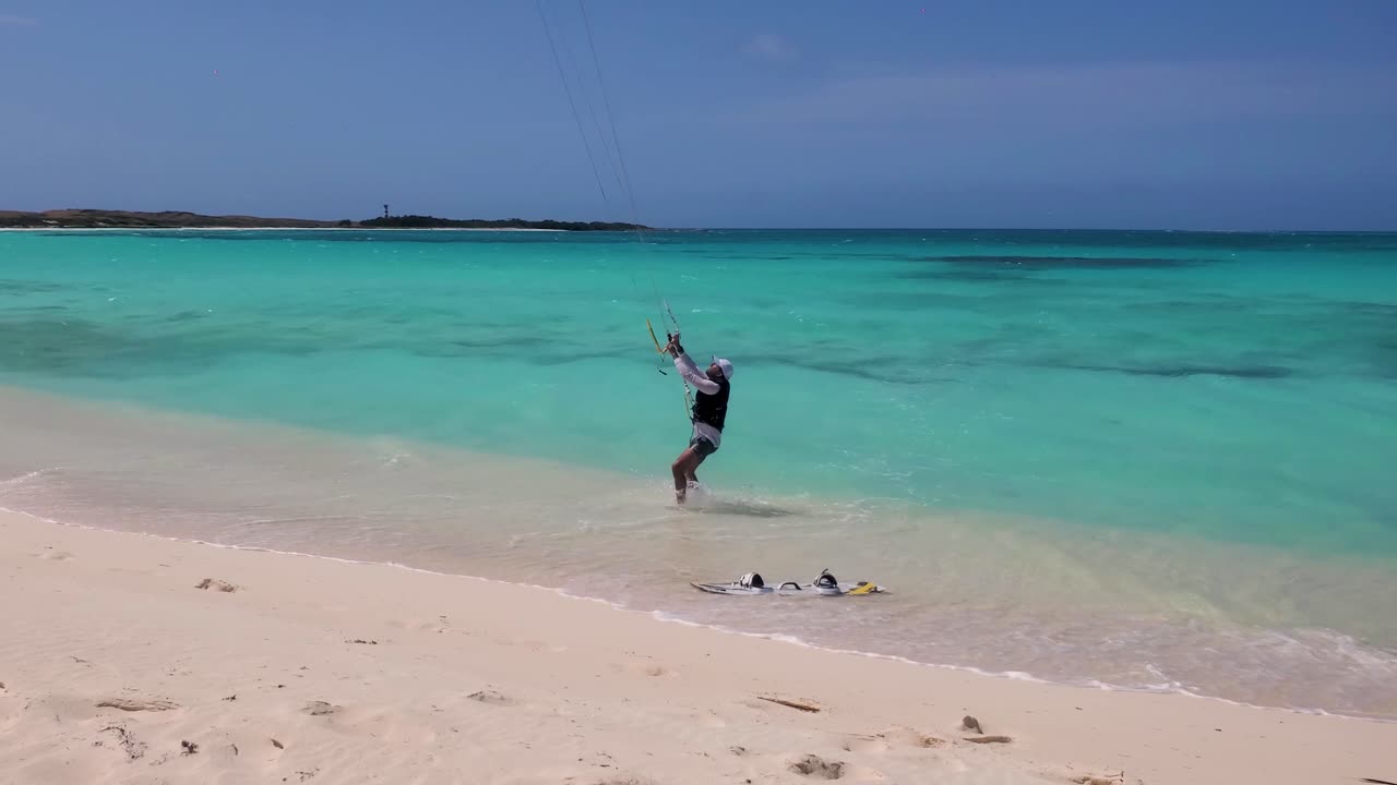 Man arrive shore beach after kitesurf, hands Steering bar and drop board on white sand