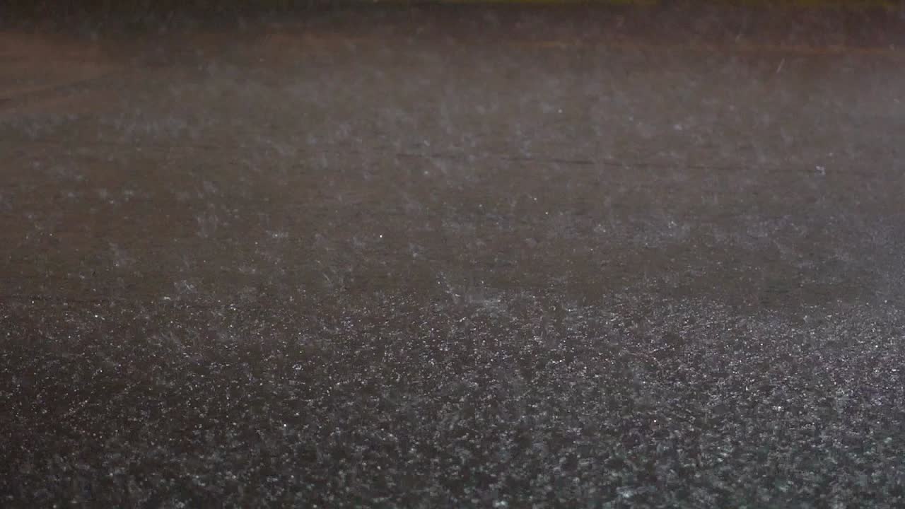 Heavy rain falls at night over a city street. Close view, slow-motion