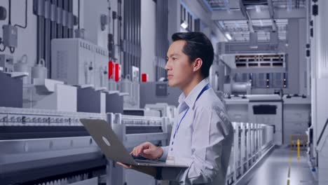 side view of an asian male professional worker standing at pharmaceutical factory, vaccine production facility, observes by looking up before he come to concentrating on the laptop and keep on typing