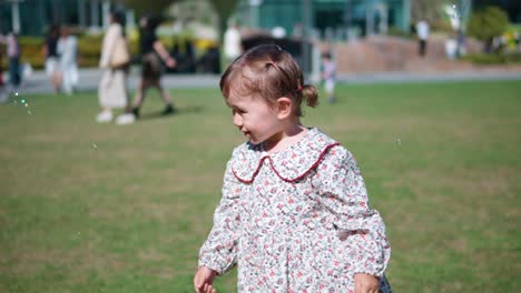 niña pequeña feliz y juguetona jugando a atrapar burbujas con las manos en un parque en un césped verde