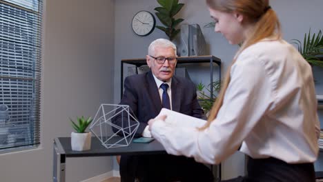 Senior-businessman-company-director-explaining-documents-discussing-project-with-woman-colleague