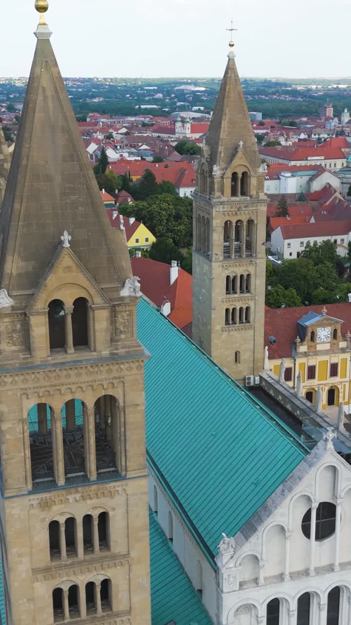 Aerial vertical orbit of Pécs Cathedral towers, capturing the historic structure and urban surroundings