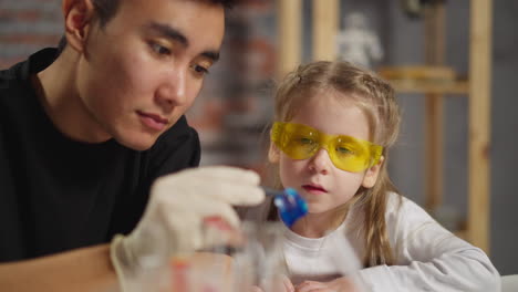 asian man teacher and girl look at blue litmus test at table