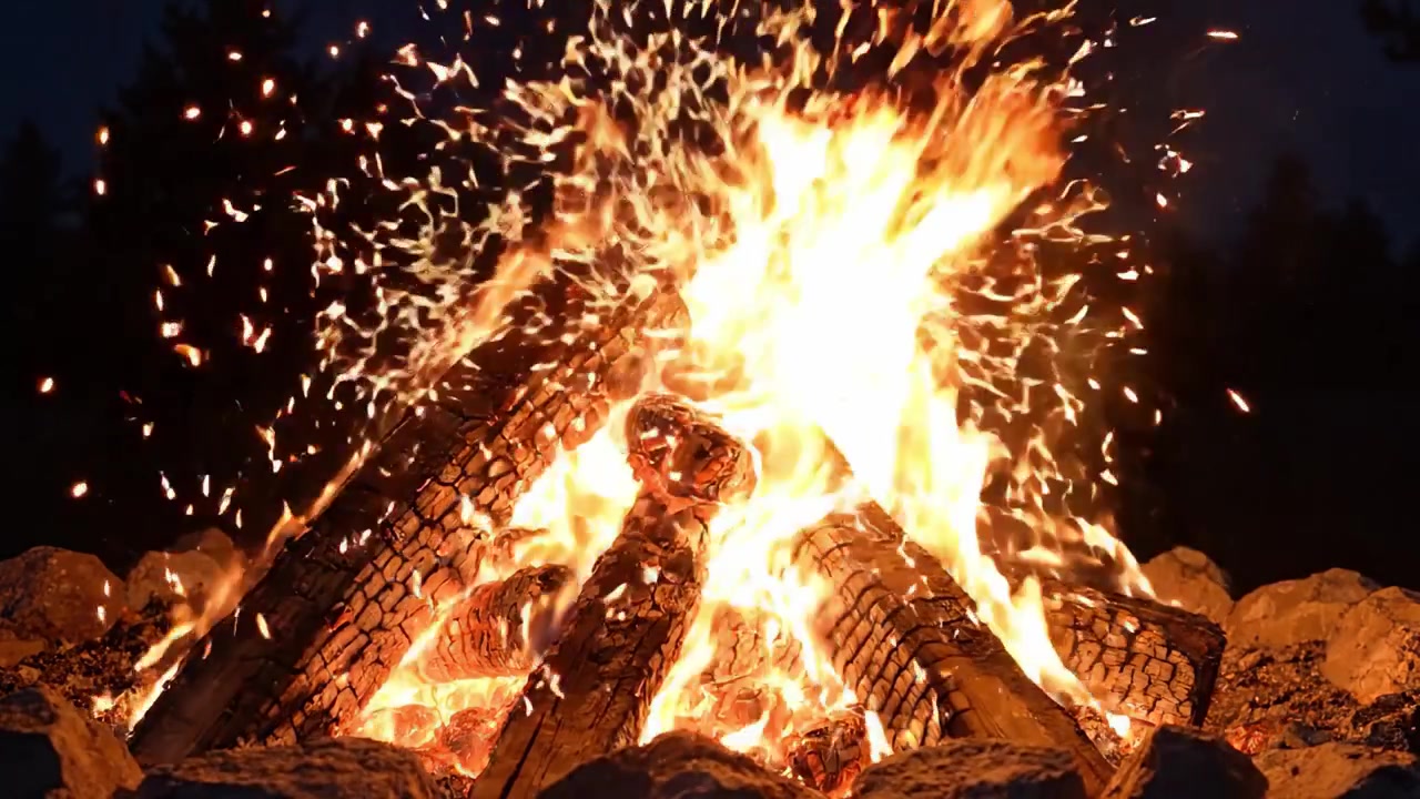 Una scena di falò ipnotizzante con fiamme scoppiettanti e braci ardenti di notte, perfetta per riunioni all'aperto e momenti accoglienti nella natura.