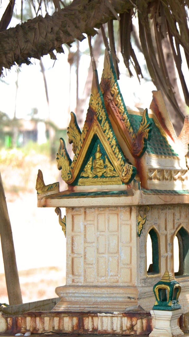 Un'inquadratura media di un santuario thailandese in miniatura per gli spiriti sotto foglie di palma tropicali