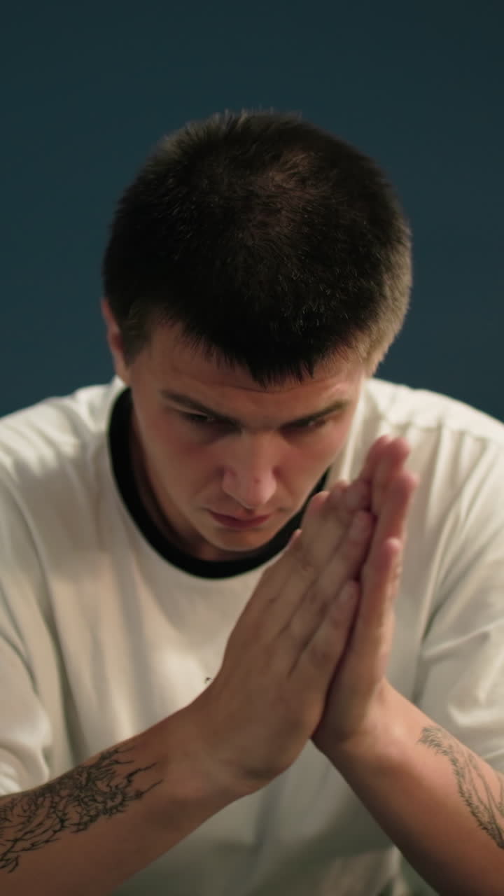 hombre de polo blanco frotándose la cara pensativamente por la noche, sentado bajo las lámparas de la calle con una persona que pasa en el fondo, mostrando un momento reflexivo de contemplación