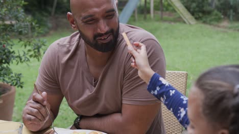 padre y hija bi-raciales felices comiendo en la mesa del jardín, cámara lenta