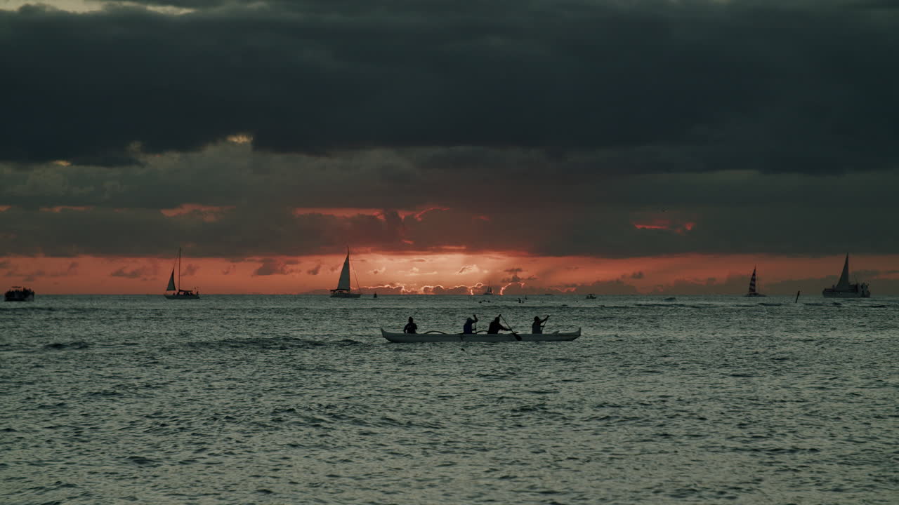 Sunset over ocean with outrigger canoe and sailboats