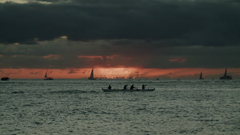 sunset over ocean with outrigger canoe and sailboats