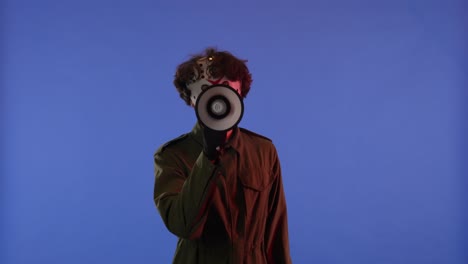 man in white mask with loudspeaker in hands on blue background with red neon light image of maniac