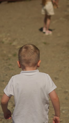 niño en edad preescolar y escolar caminan a lo largo de la orilla arenosa vista trasera. niño pequeño corre alcanzando a su hermana. pareja de niños se divierten juntos en la naturaleza en cámara lenta