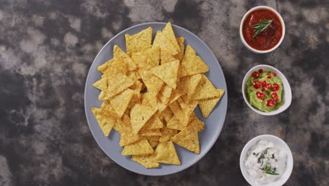 close up of nachos in a plate and sauces on black surface