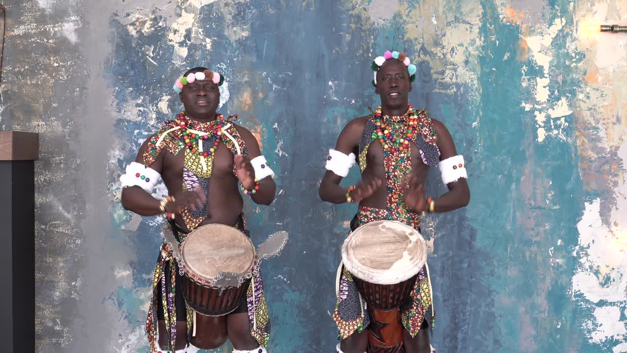 Two African artists in colorful costumes playing djemba drums