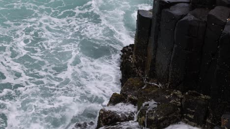 waves impact against basalt columns by the sea