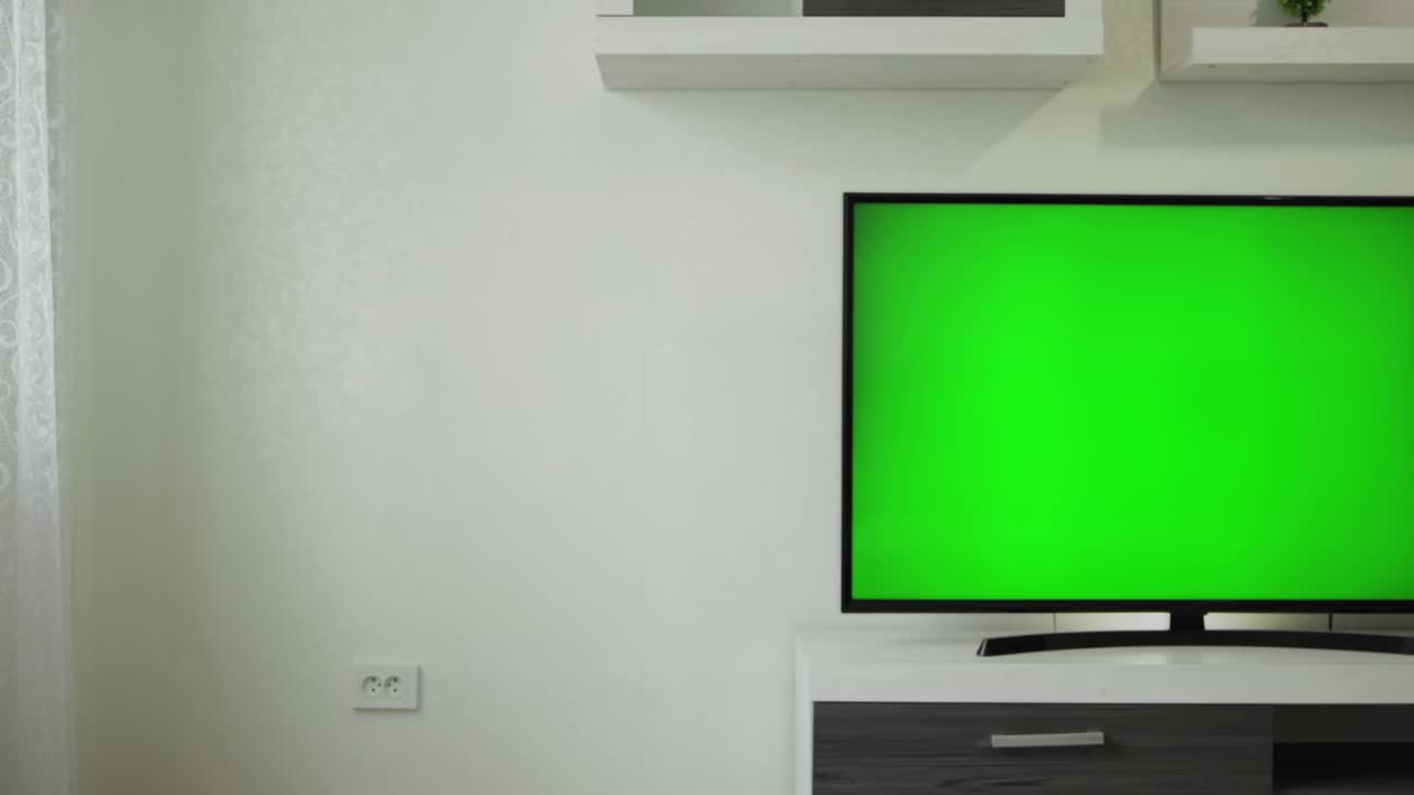 Slider truck shot of lcd TV 55 inches with green screen chromakey in empty modern interior apartment. Streaming broadcast. Nobody, no one in living room. Furniture. Wide shot