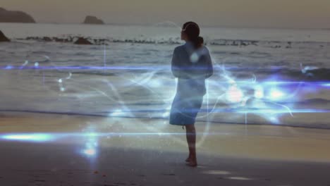 Animation-of-light-trails-over-caucasian-woman-walking-on-beach