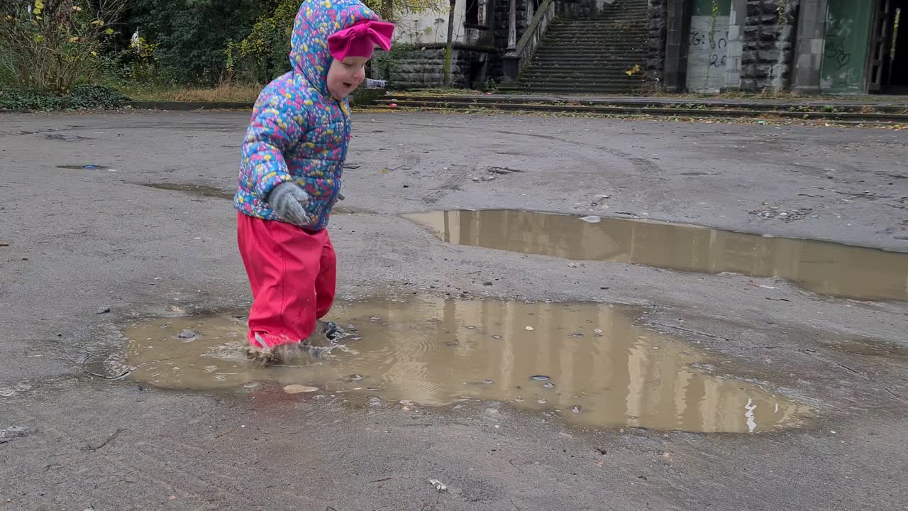 Happy baby is jumping in mud puddle and dirty water splashes