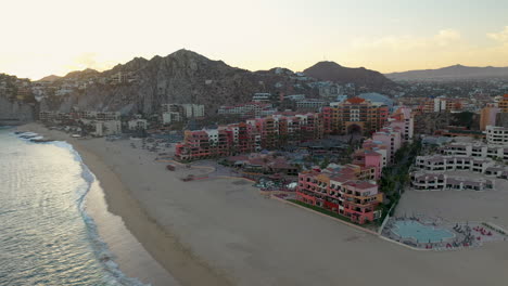 Drone-shot-of-resort-hotel-on-Playa-El-Médano-with-mountains-in-the-distance-in-Cabo-San-Lucas-Mexico,-wide-and-rotating