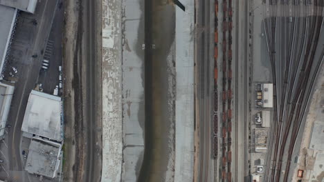 AERIAL:-Overhead-,-Birds-Eye-View-on-Los-Angeles-River-with-Water-on-Cloudy-Overcast-Sky-next-to-Train-Tracks