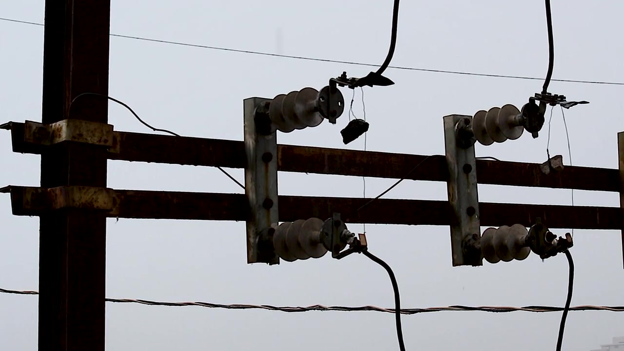 Close-up footage of rain falling on high-voltage power line insulators at electrical substation. Ideal for energy, utility, infrastructure, engineering, weather and power grid projects.