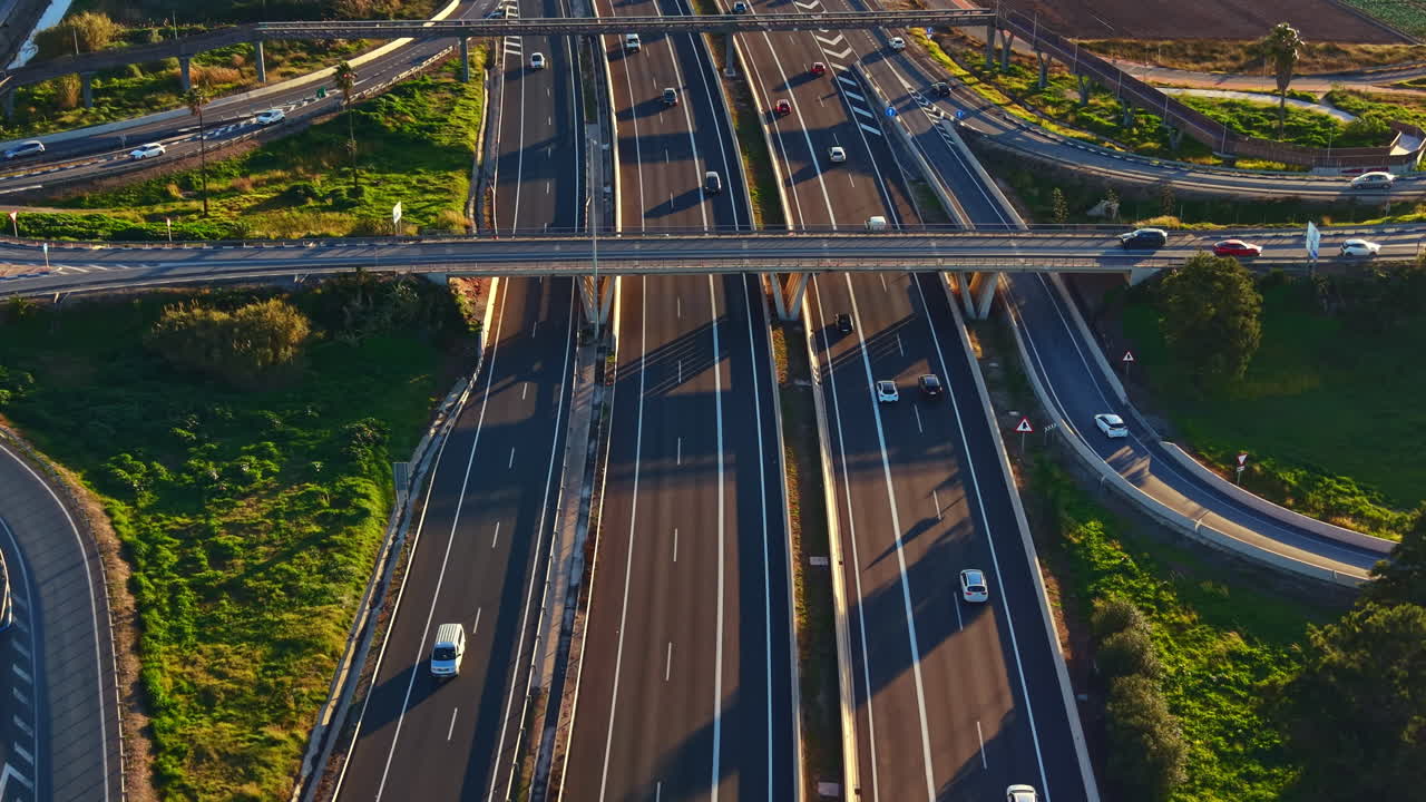 Highway with multiple lanes and vehicles traveling at sunset near a green area and fields