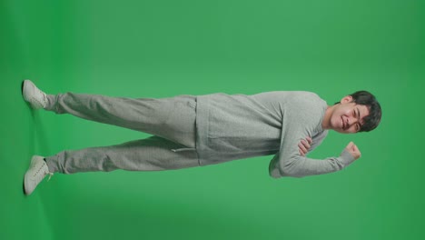 cuerpo lleno de un hombre asiático sonriente flexiona el músculo mientras está de pie frente al fondo de la pantalla verde