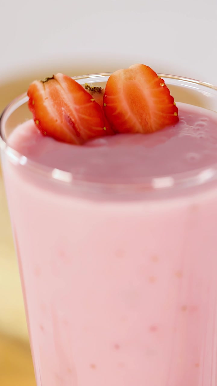 Batido de fresa rosa en vaso alto, cubierto con rodajas frescas, acercamiento lento de cámara, iluminación brillante