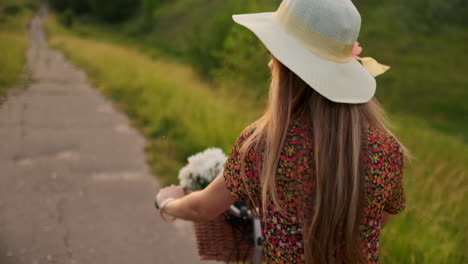 A-girl-in-a-dress-riding-a-bike-with-flowers-in-a-basket-and-laughing-enjoying-the-freedom-and-summer-air.-Slow-motion.