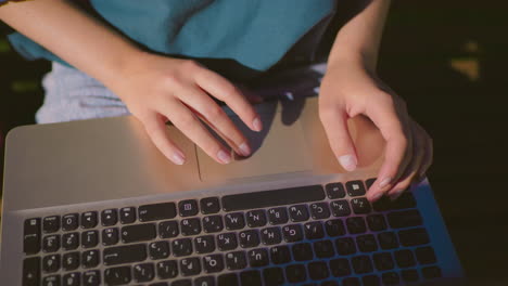 close-up of typist typing on laptop outdoors at night with hands illuminated by screen glow, denim jeans subtly reflect on laptop surface, with red bag by the side